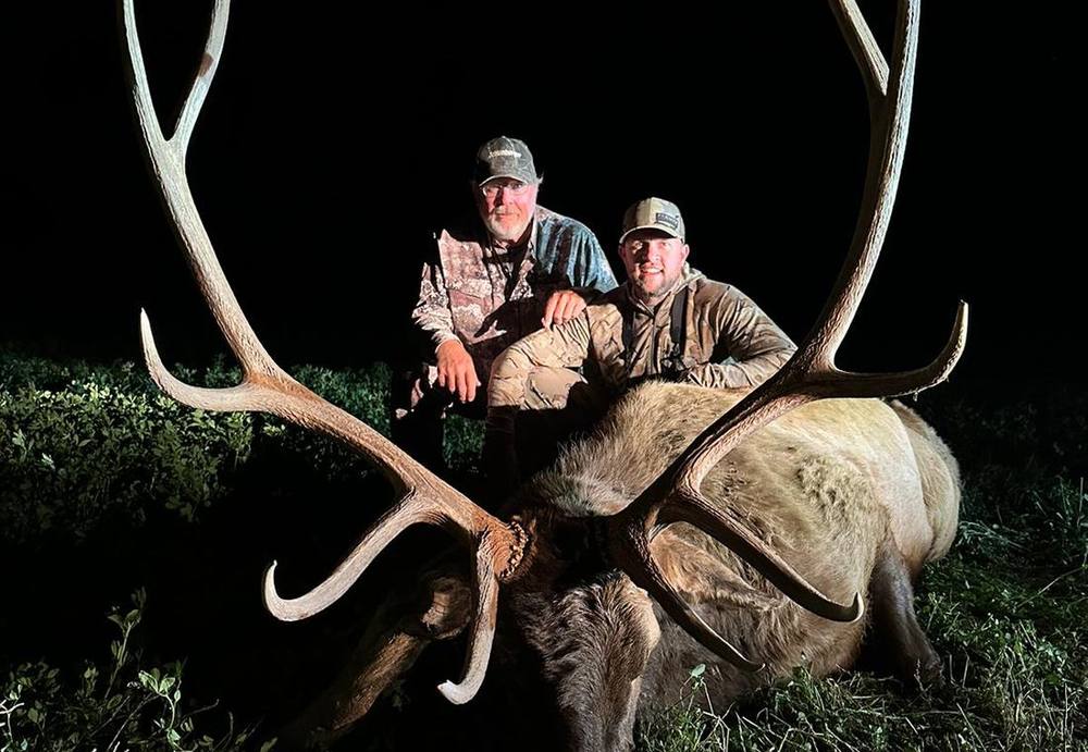 Two hunters with a heavy bull elk photographed after an evening hunt