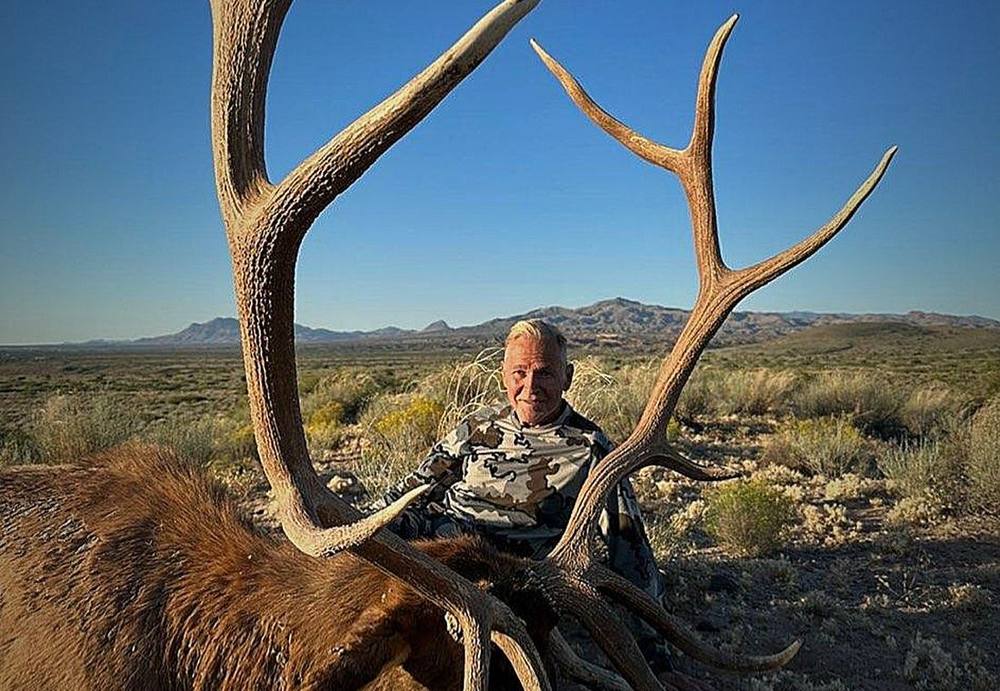Bull elk and hunter on an open desert flat below the mountains