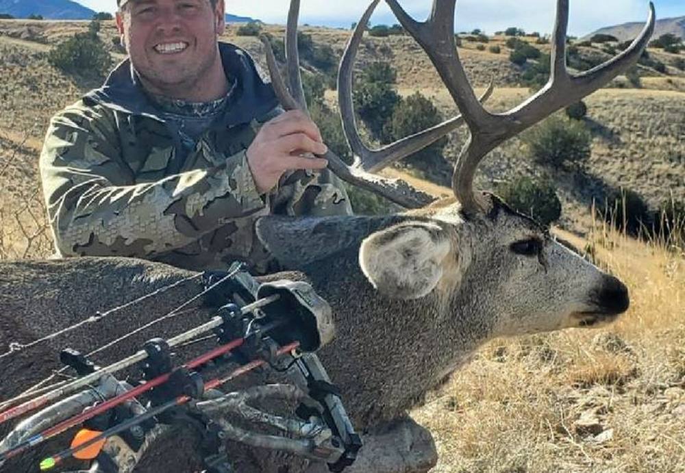 Hunter with a heavy-beamed mule deer buck and a crossbow in the New Mexico desert