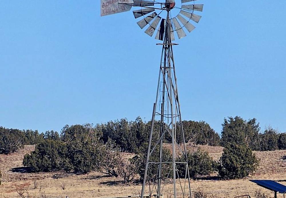Windmill and stock tank standing over the dry grass of the ranch